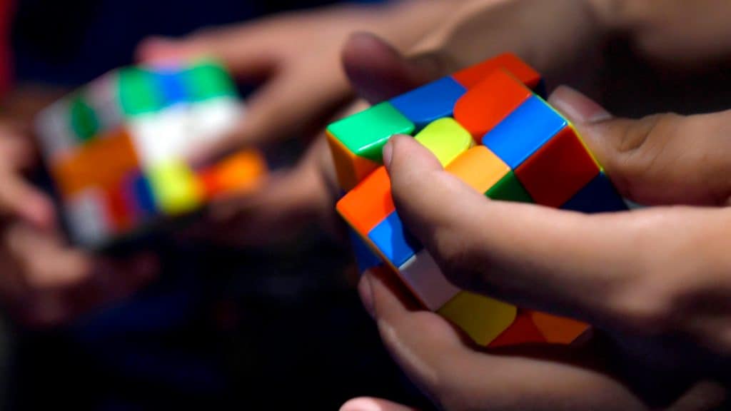 Imagem de mãos de duas pessoas resolvendo cubo mágico, ilustrando a importância do cubo mágico na volta às aulas 