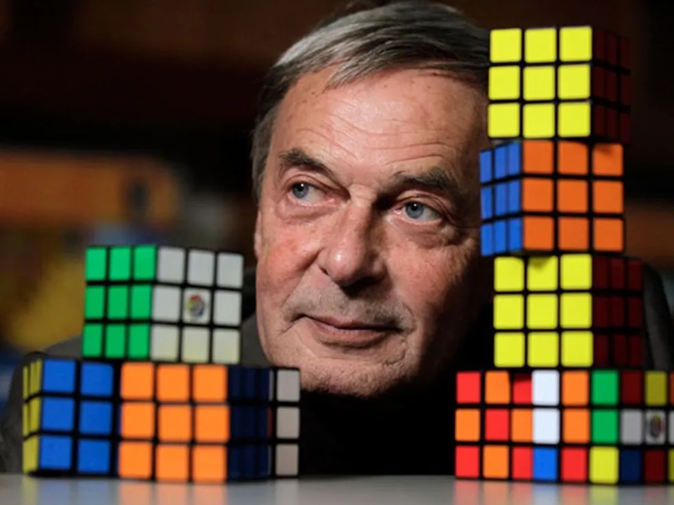 Imagem de Ernõ Rubik, criador do cubo mágico com vários cubos mágicos