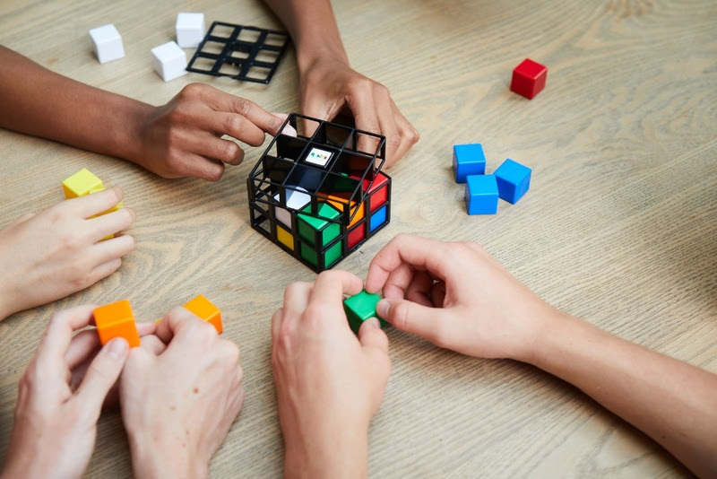 Imagem de três pessoas montando um cubo 3x3x3, cubo que estará presente nas competições de janeiro de 2024