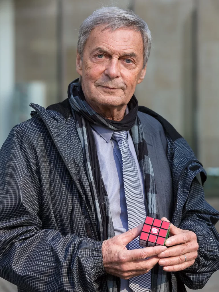 Imagem de Ernõ Rubik segurando um cubo 3x3x3, modelo que está completando 50 anos em 2024